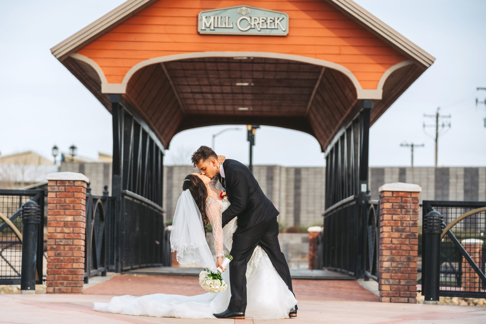 Novios compartiendo un beso bajo la entrada de Mill Creek